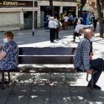 Dos ciudadanos sentados en un banco manteniendo la distancia de seguridad, en la calle Mossen Jacint Verdaguer de Santa Coloma de Gramanet (Barcelona), en plena área metropolitana.