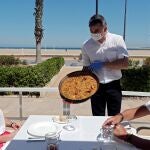 Un camarero sirve una paella en una terraza de un restaurante de la playa de la Malvarrosa de Valencia