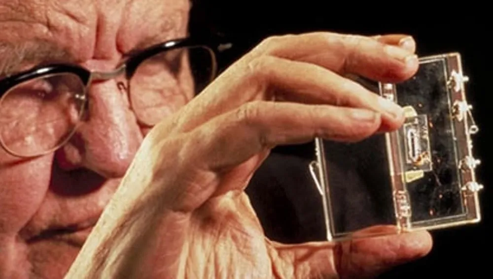 Jack Kilby sosteniendo un microchip moderno, la versión en miniatura de su invento.