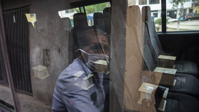 Piedrangel funeral home worker Anibal Rosado is reflected in a window of a company van as he prepares to help deliver to relatives, urns that contain the cremated ashes of people who are suspected to have died from the new coronavirus, in Lima, Peru, Monday, May 4, 2020. Edgard Gonzales, who owns the funeral home with his three brothers, says Piedrangel cremates all COVID-19 victims. (AP Photo/Rodrigo Abd)