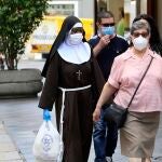 Varias personas, entre ellas una monja con mascarillas y guantes, recorren por el centro de Sevilla