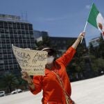 A demonstrator holds up a sign calling for the resignation of President Andres Manuel Lopez Obrador, as she stands along the road during a anti-government driving protest by hundreds of cars, in Mexico City, Sunday, June 28, 2020. (AP Photo/Rebecca Blackwell)