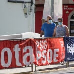 Dos personas protegidas con mascarilla pasean junto a carteles electorales del PPdeG y del PSdeG en Foz, en la comarca de A Mariña, Lugo, Galicia (España), a 9 de julio de 2020. El pasado 5 de julio la Xunta ordenó el cierre hasta mañana 10 de julio de los accesos del distrito sanitario que comprende a los municipios de Alfoz, Barreiros, Burela, Cervo, Foz, Lourenzá, Mondoñedo, Ourol, Ribadeo, Trabada, O Valadouro, O Vicedo, Viveiro y Xove. La finalidad del confinamiento es controlar la transmisión del coronavirus en la comarca de A Mariña lucense, donde se han elevado a 144 los casos activos en el brote registrado.09 JULIO 2020Carlos Castro / Europa Press09/07/2020