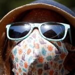 Una niña con mascarilla y con sombrero para protegerse del calor