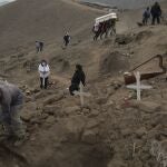 FILE - In this May 27, 2020, file photo, a cemetery worker shovels dirt into a grave that contains the remains of Apolonia Uanampa, who died from the coronavirus, as the coffin that contains the remains of Demetria Huamani, also a victim of the virus, is carried to her burial site at the Nueva Esperanza cemetery on the outskirts of Lima, Peru. A new snapshot of the frantic global response to the coronavirus pandemic shows some of the world's largest government donors of humanitarian assistance are buckling under the strain and overall aid commitments have dropped by a third from the same period last year. (AP Photo/Rodrigo Abd, File)