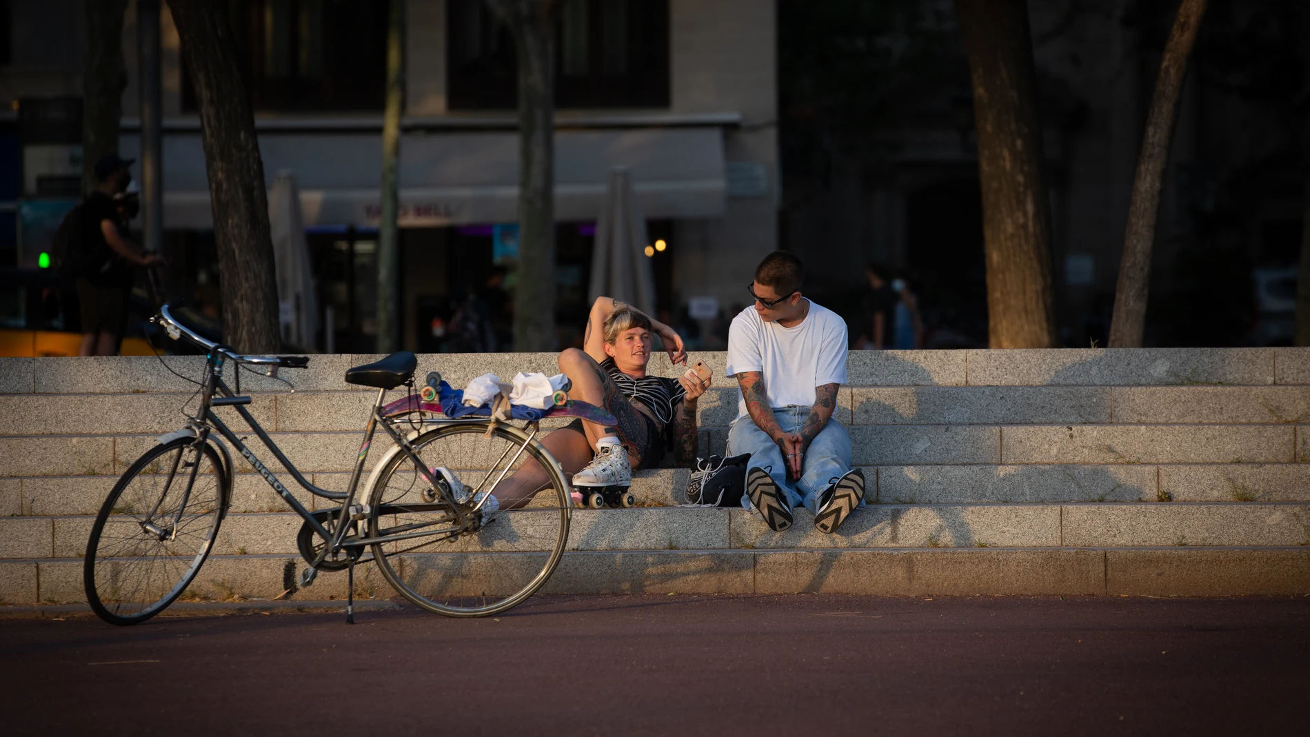 Dos jóvenes descansan junto a una bicicleta en Barcelona