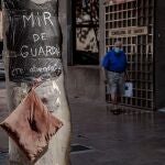 Una persona pasa ante la Consellería de Sanidad donde se puede ver una bolsa de basura usada a modo de bata con el lema "MIR de guardía ¿Te atiendo?" colgada de un arból, donde un grupo de médicos internos residentes (MIR) ha pasado esta noche al raso en el marco de la huelga indefinida que este colectivo mantiene para reivindicar mejores condiciones laborales.