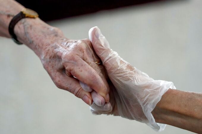 Una hija y una madre que permanece en una residencia de ancianos se dan la mano