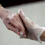 Una hija y una madre que permanece en una residencia de ancianos se dan la mano