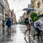 Una madre con paraguas, con un carrito de bebe protegido para la lluvia