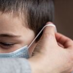 Una madre coloca a su hijo una mascarilla.
