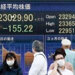 Tokio: Personas con mascarillas para evitar la propagación del coronavirus pasan por delante de un tablero electrónico que muestra la media bursátil japonesa Nikkei