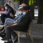 Varias personas descansan en un banco protegidos con mascarilla en León
