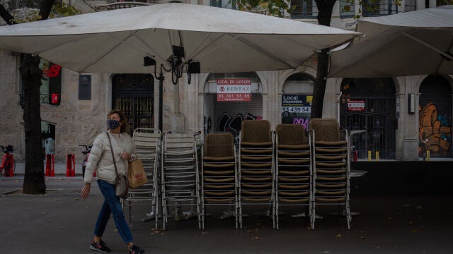 Una mujer pasa junto a la terraza recogida de un bar cerrado durante el cuarto día de la entrada en vigor de las nuevas restricciones en Cataluña, en Barcelona, Cataluña (España) a 20 de octubre de 2020. El pasado viernes 16 de octubre entraron en vigor las nuevas restricciones decretadas por la Generalitat por el coronavirus. Entre ellas, se paraliza la actividad durante dos semanas en bares restaurantes, se suspende la actividad deportiva no profesional dos semanas, se cierran las áreas de juego infantil a las 20.00h, se suspende la apertura al público de juegos, casinos y bingos, se reduce el 50% del aforo en zonas comunes de hoteles y también en cines y restaurantes, y se reduce al 30% el aforo en comercios superiores a 400 metros cuadrados y centros comerciales.20 OCTUBRE 2020 CORONAVIRUS;COVID-19;PANDEMIA;ECONOMÍA;CRISISDavid Zorrakino / Europa Press20/10/2020