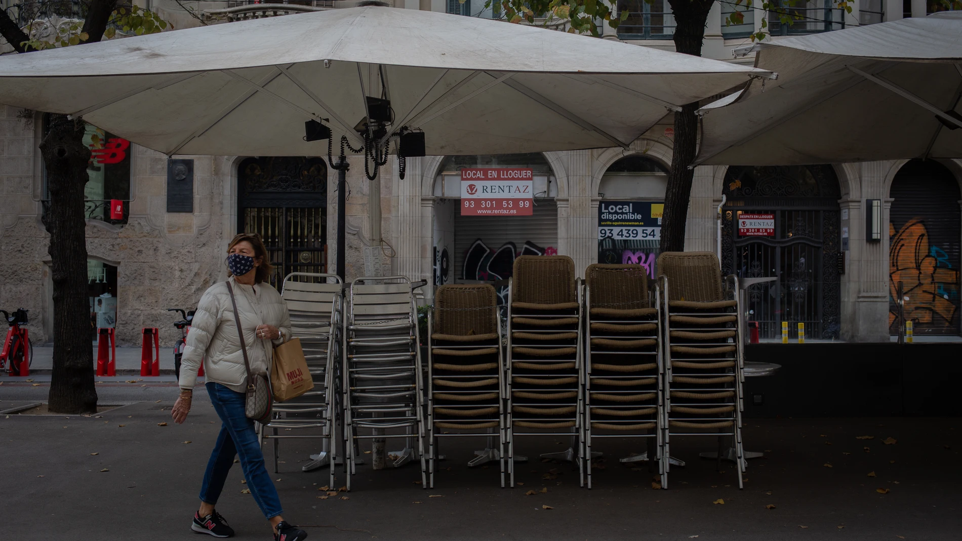 Una mujer pasa junto a la terraza recogida de un bar cerrado durante el cuarto día de la entrada en vigor de las nuevas restricciones en Cataluña, en Barcelona, Cataluña (España) a 20 de octubre de 2020. El pasado viernes 16 de octubre entraron en vigor las nuevas restricciones decretadas por la Generalitat por el coronavirus. Entre ellas, se paraliza la actividad durante dos semanas en bares restaurantes, se suspende la actividad deportiva no profesional dos semanas, se cierran las áreas de juego infantil a las 20.00h, se suspende la apertura al público de juegos, casinos y bingos, se reduce el 50% del aforo en zonas comunes de hoteles y también en cines y restaurantes, y se reduce al 30% el aforo en comercios superiores a 400 metros cuadrados y centros comerciales.20 OCTUBRE 2020 CORONAVIRUS;COVID-19;PANDEMIA;ECONOMÍA;CRISISDavid Zorrakino / Europa Press20/10/2020