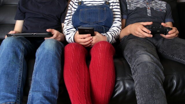 Tres niños con diferentes pantallas: tableta, móvil y un mando de videojuegos