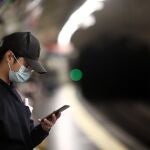 Un joven mira su móvil mientras espera la llegada del metro en la estación de Estrecho, en el distrito de Tetúan, en Madrid