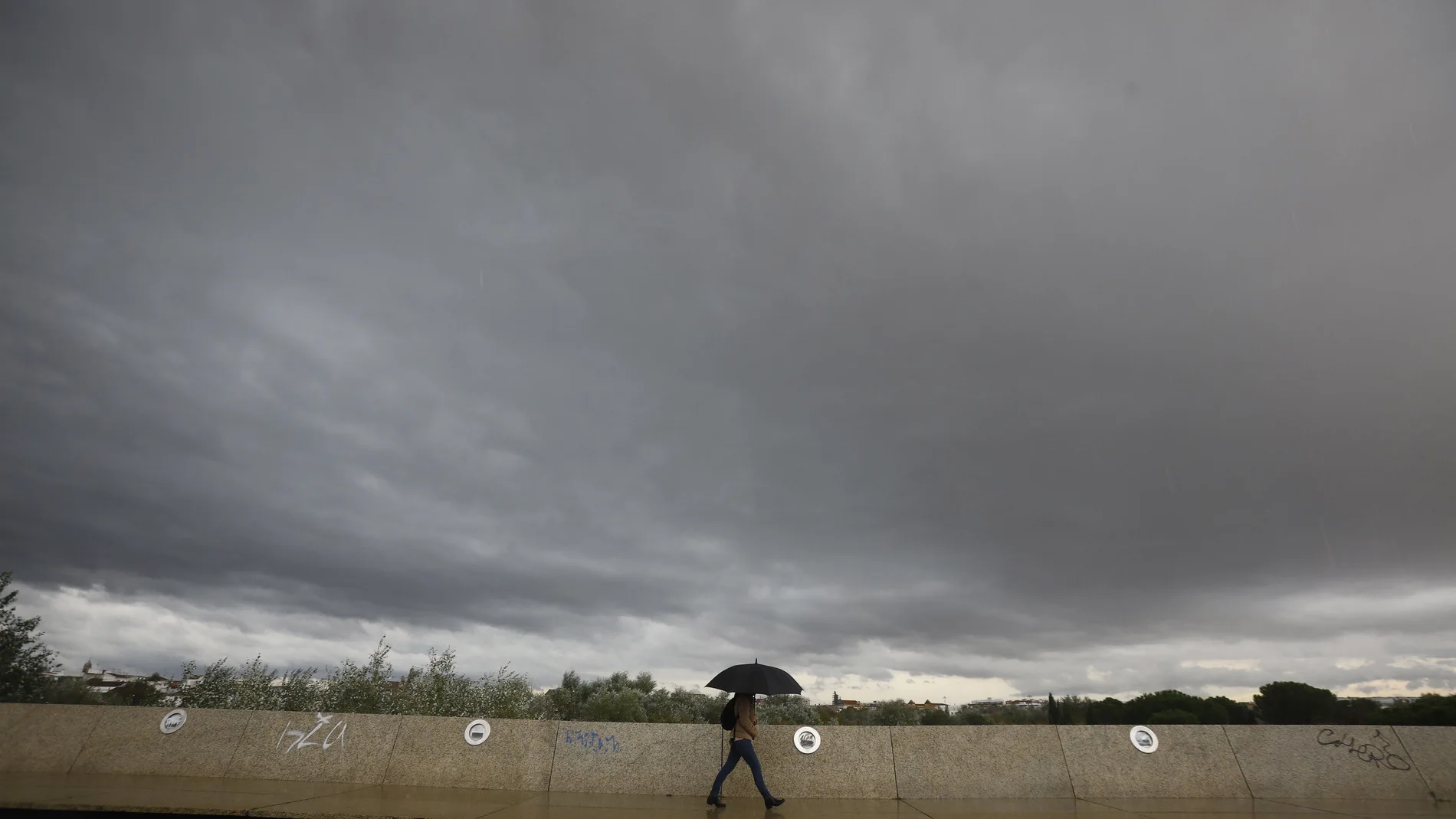 Una persona se resguarda de la lluvia con un paraguas bajo un cielo negro en Córdoba