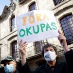 Una mujer sostiene una cartel con la frase "fuera okupas"