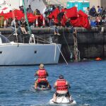 Dos turistas en motos de agua pasan junto al muelle de Arguineguín, donde se hacinan más de 1.700 inmigrantes