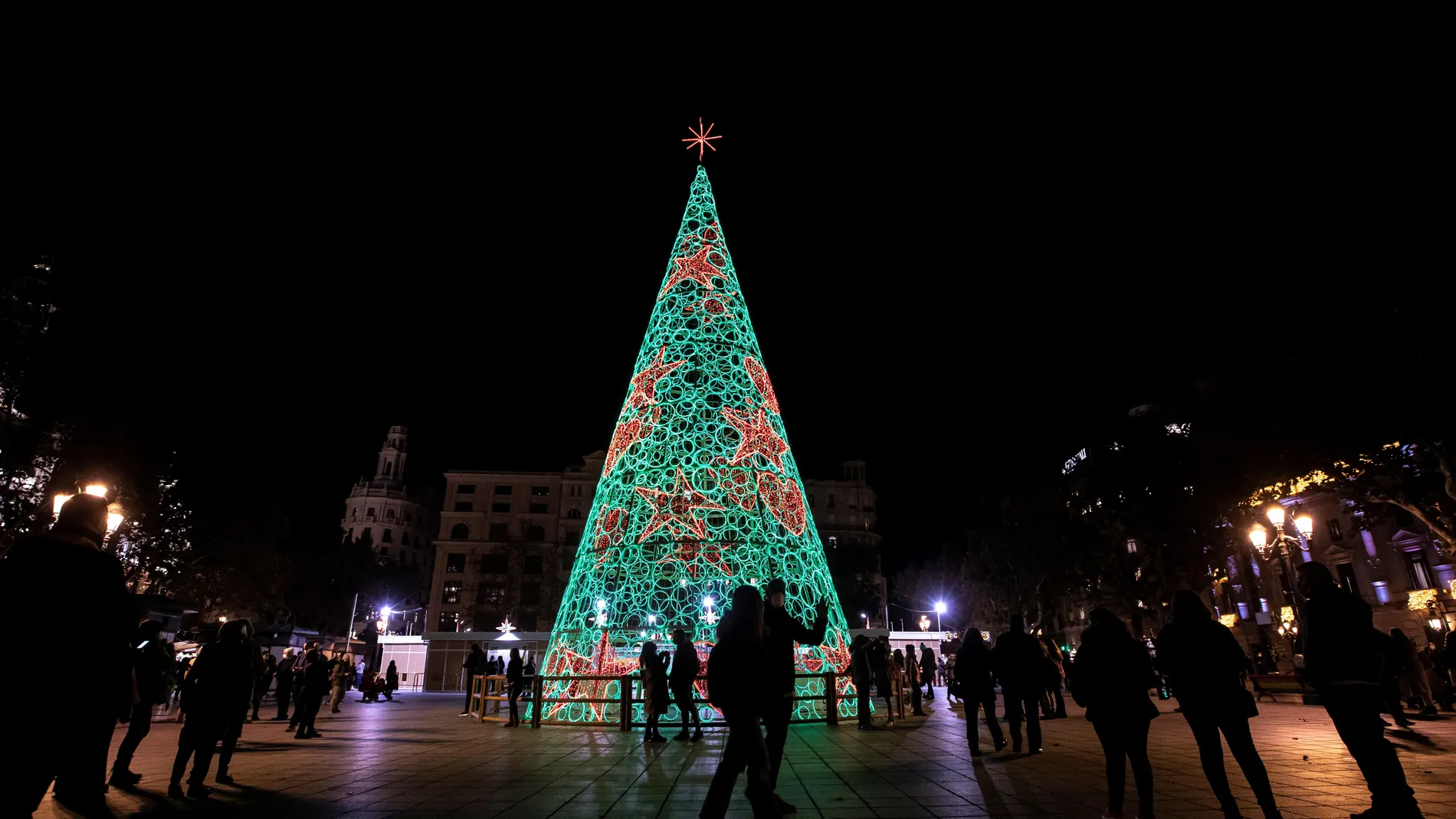 Varias personas pasean frente al árbol de navidad iluminado tras el acto de encendido de luces del ayuntamiento de València. EFE/Biel Aliño
