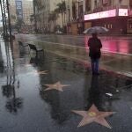 A woman waits at a bus stop in the rain Monday, Dec. 28, 2020, in the Hollywood section of Los Angeles. Rain, hail and snow fell Monday as Southern California saw its first significant storm of the season. (AP Photo/Marcio Jose Sanchez)