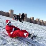 Un hombre disfrazado de Papá Noel se tira en trineo por el lienzo norte de la muralla de Ávila este viernes