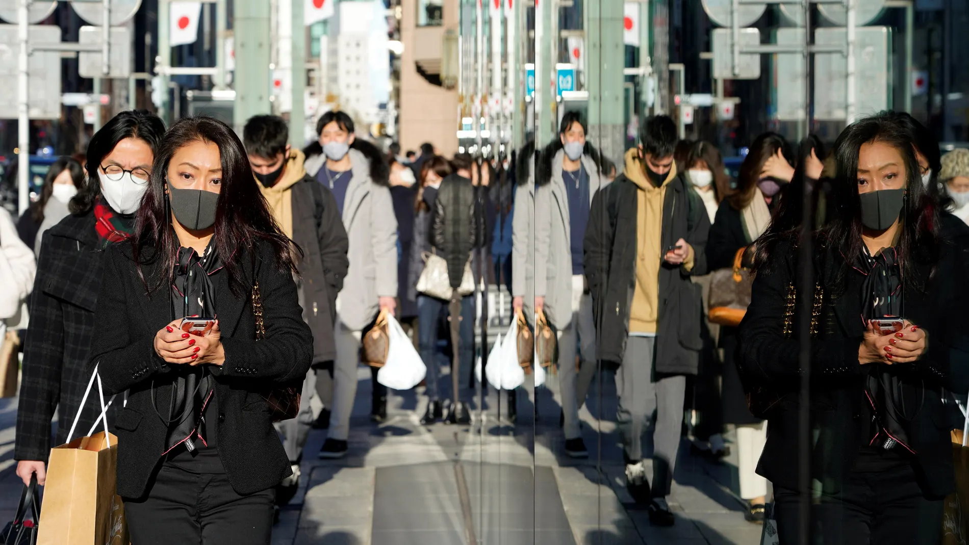 unos peatones con mascarillas se reflejan en un escaparate del distrito comercial de Ginza en Tokio, Japón