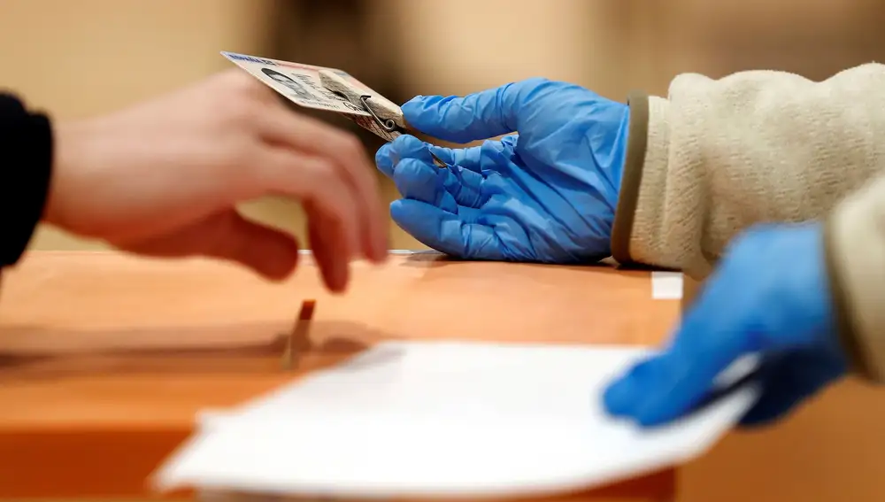 La presidenta de una mesa electoral sostiene el DNI de un votante en las elecciones catalanas del 14 de febrero. En Madrid, los electores colocarán su documento en una bandeja antes de votar