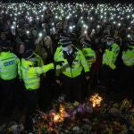 Los asistentes a una vigilia en memoria de Sarah Everard encienden las linternas de sus teléfonos móviles tras un cordón formado por agentes de la Policía Metropolitana de Londres (MET) , la noche del sábado en Clapham Common, Londres.