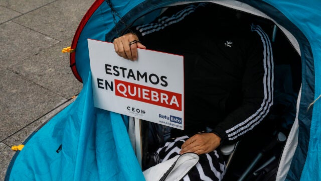 Un trabajador del ocio nocturno con un cartel en el que se lee: "Estamos en quiebra", participa en una concentración hoy en la plaza de Manises de Valencia