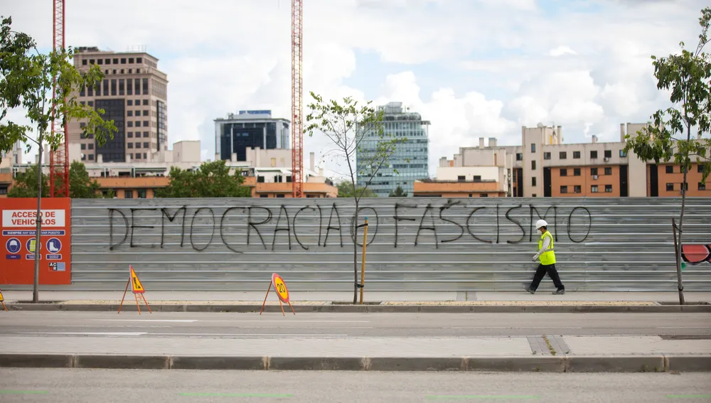 Imagen de un obrero pasando por una pintada en la que se puede leer "democracia o fascismo"