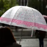Una mujer bajo la lluvia con su paraguas cruza un paso de peatones en Madrid