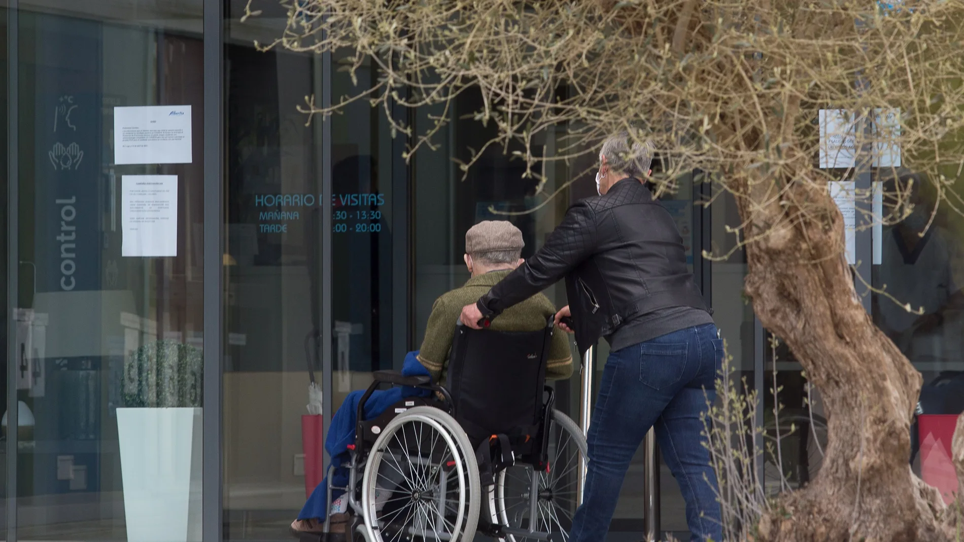 Una mujer pasea junto a un anciano en silla de ruedas