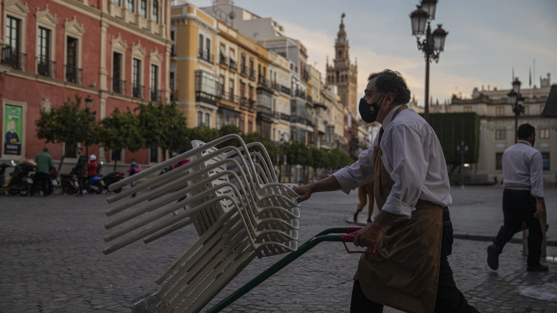 Un camarero recoge el mobiliario de la terraza de un bar en Sevilla