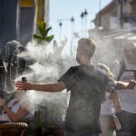 Un chico se refresca del calor con un difusor de vapor de agua de un restaurante
