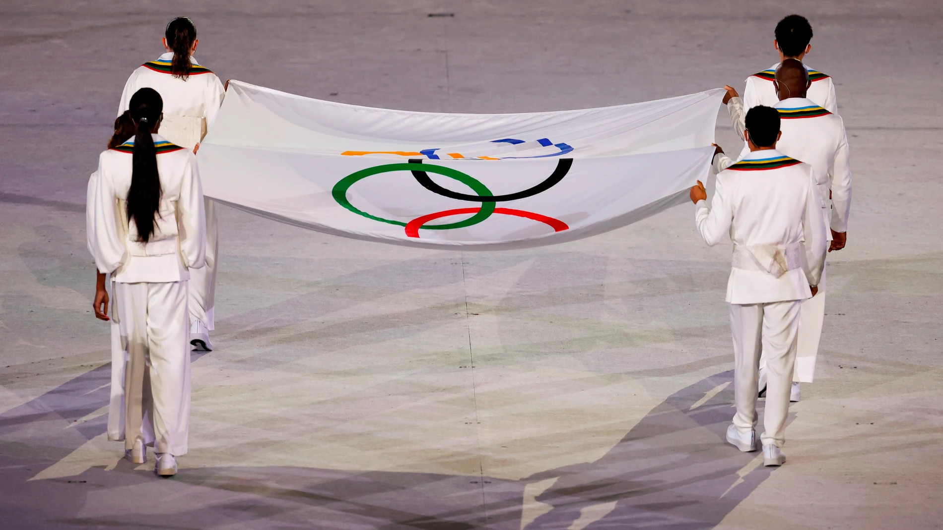 Operarios portan la Bandera Olímpica durante la ceremonia inaugural de los Juegos Olímpicos de Tokio 2020
