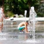 Dos niños juegan en una fuente para mitigar el intenso calor.