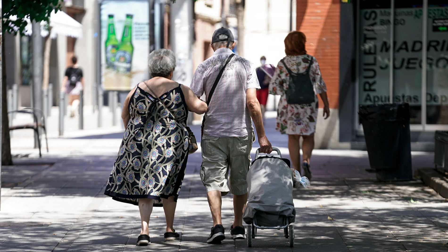 Una pareja mayor camina por la calle con un carro de compra