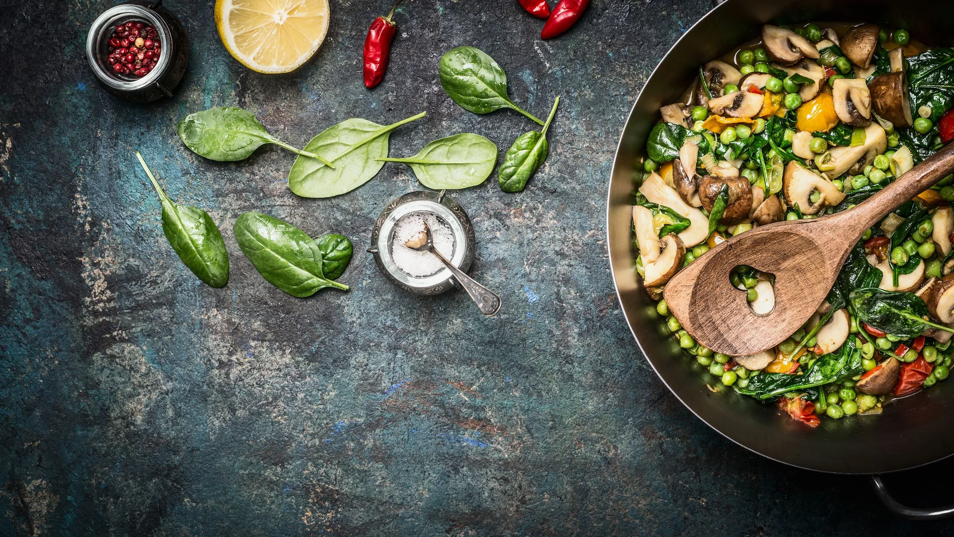 Colorful steamed healthy vegetables in cooking pot with ingredients on rustic background, top view. Vegetarian food or diet nutrition concept