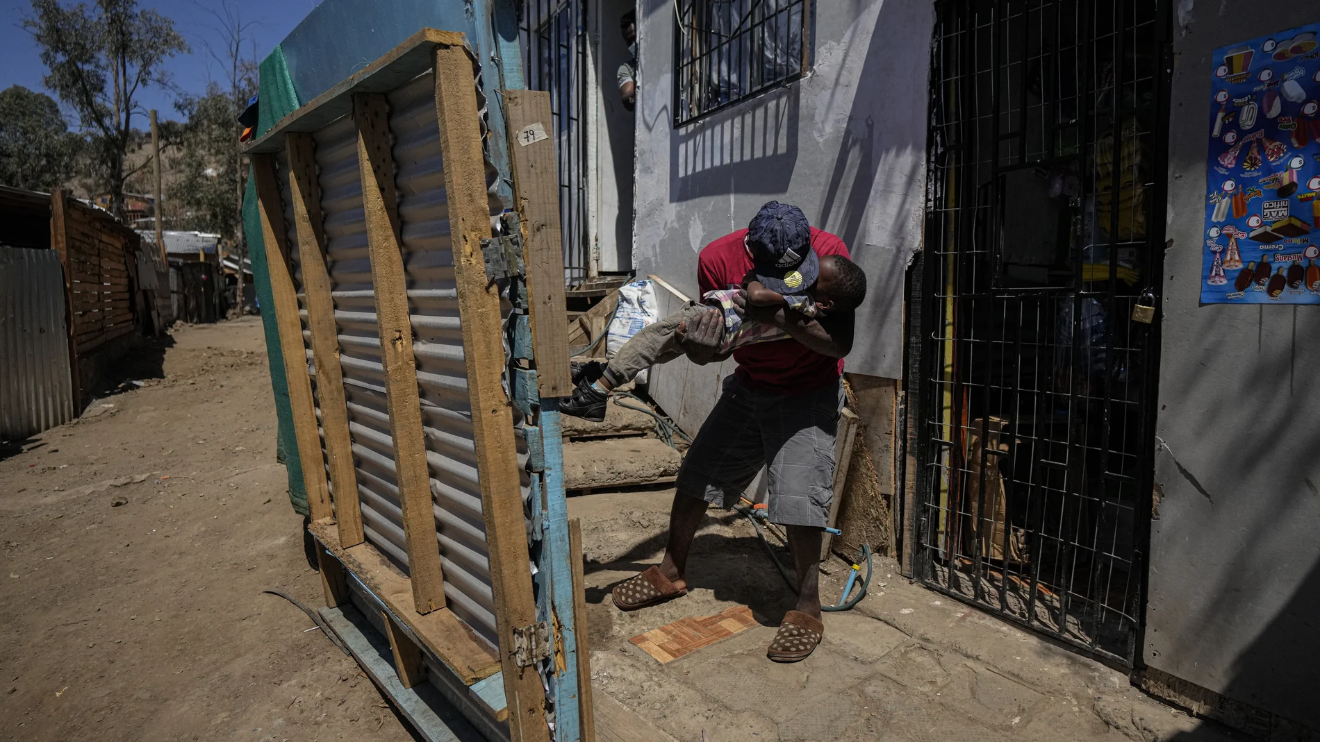 Haitian Edanold Delva, who has permanent residency in Chile, plays with his Chilean-born son Moises, 2, outside their home they share with Delva wife, Moises' mother, Jacqueline Michel, who also has residency, in the Bosque Hermoso camp settled by migrants in Lampa, Chile, Friday, Oct. 1, 2021. Most Haitians are fleeing earthquakes, hurricanes, political turbulence and poverty in their homeland. (AP Photo/Esteban Felix)