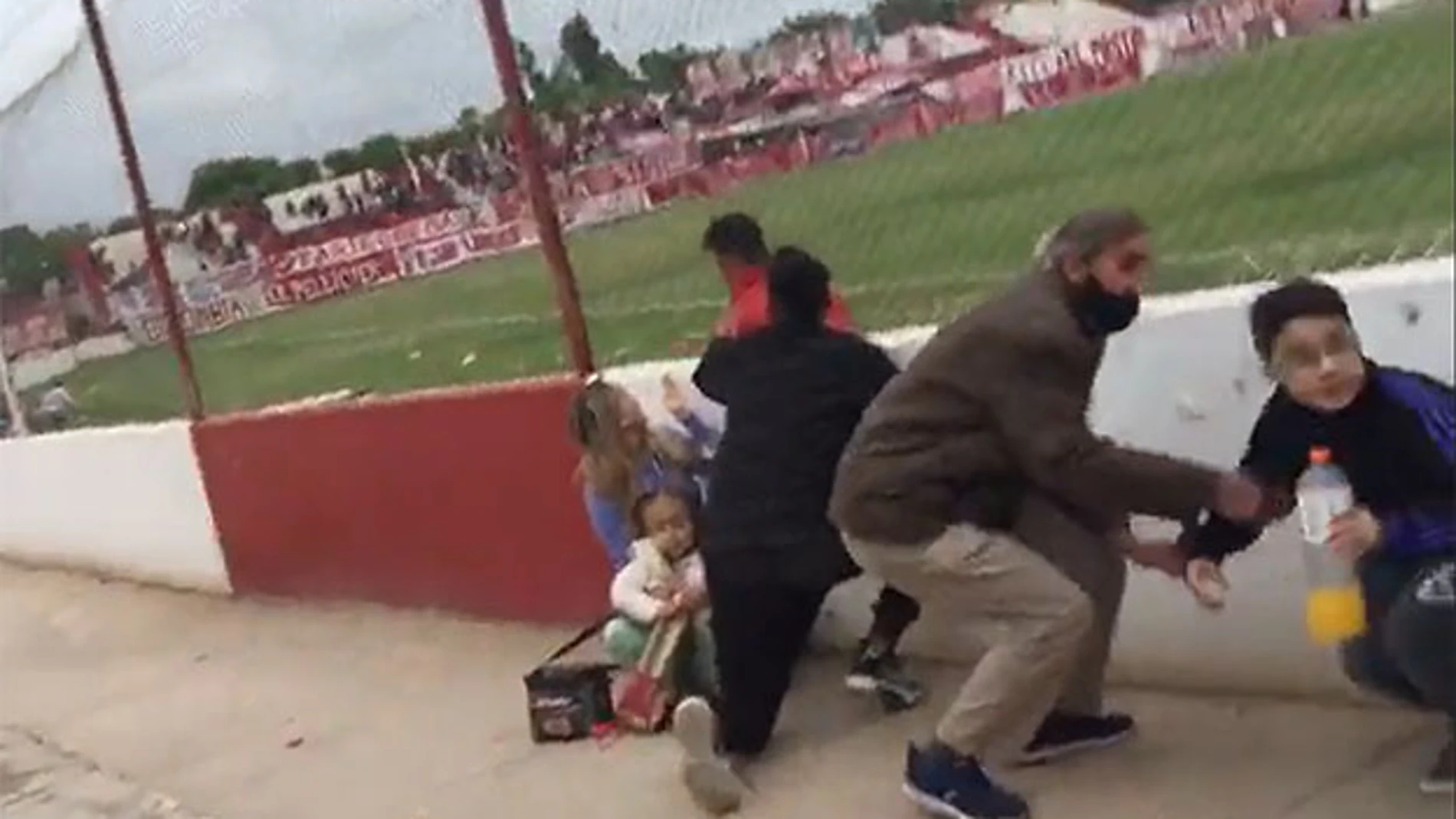 Los espectadores, entre ellos varios niños, se resguardan durante el tiroteo durante el partido entre Huracán Las Heras y Ferro de General Pico.