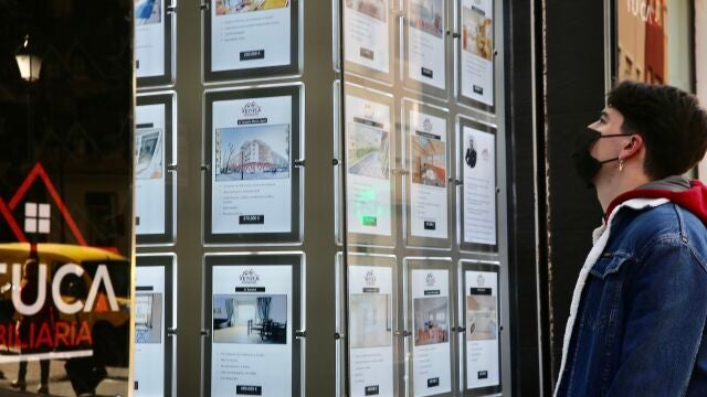 En la imagen, una persona observando el escaparate de una agencia inmobiliaria