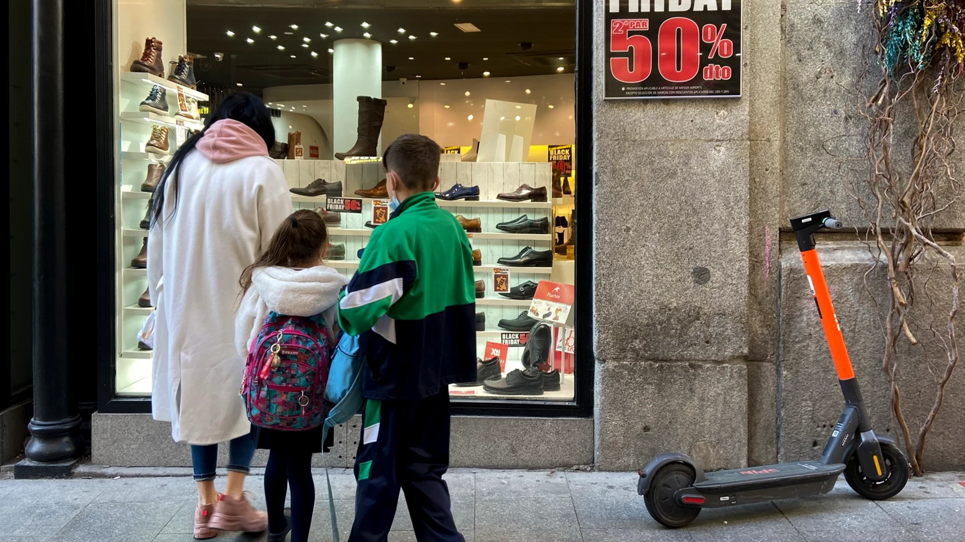 Varias personas en el escaparate de un comercio que anuncia descuentos del 50% por el Black Friday