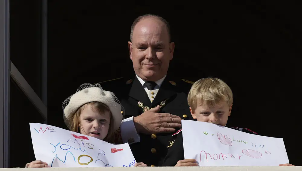 Prince Albert II of Monaco looks at his children Prince Jacques and Princess Gabriella showing messages for their mother Princess Charlene, from the balcony of the the Monaco Palace during ceremonies marking National Day, Friday Nov.19, 2021 in Monaco. Princess Charlene is currently convalescing in a confidential place after battling with poor health over the past few months. (AP Photo/Daniel Cole)