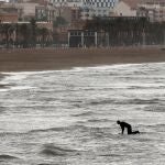 Una persona practica surf en la playa de la Malvarosa, prácticamente desierta.