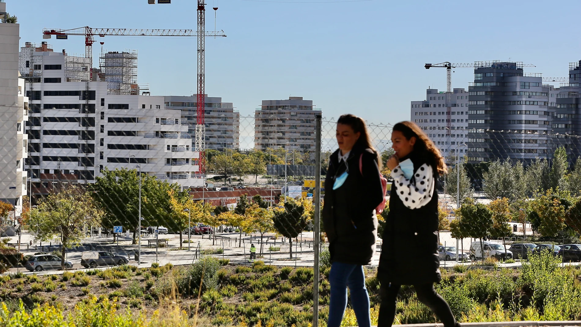 Dos jóvenes pasan por delante de varias promociones de viviendas en construcción