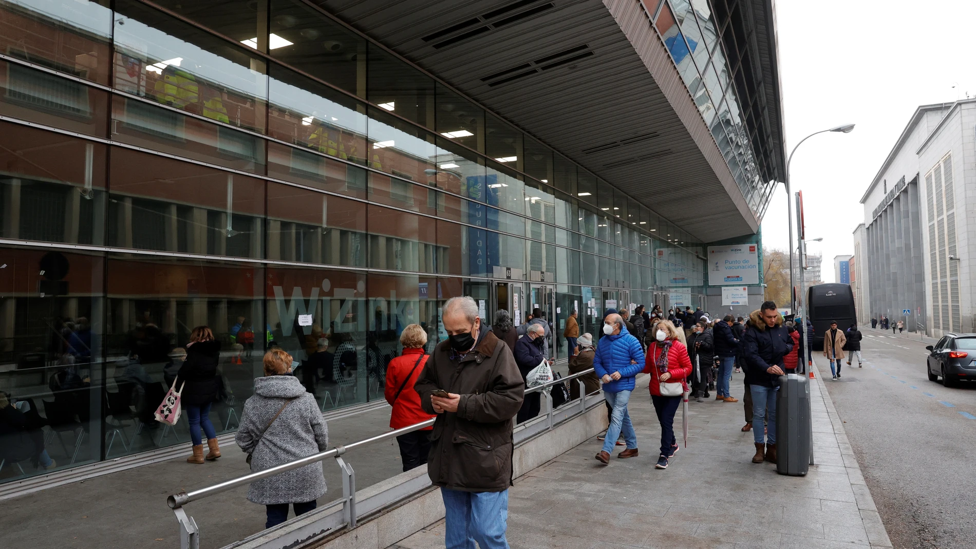Diversas personas hacen cola a las puertas del recinto Wizink Center donde se administran las vacunas frente a la Covid-19 en plena sexta ola