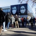 Decenas de ciudadanos guardan su turno en cola para acceder al centro de vacunación instalado en la Fira de Barcelona, hoy lunes, primer aniversario del inicio de la vacunación contra la Covid