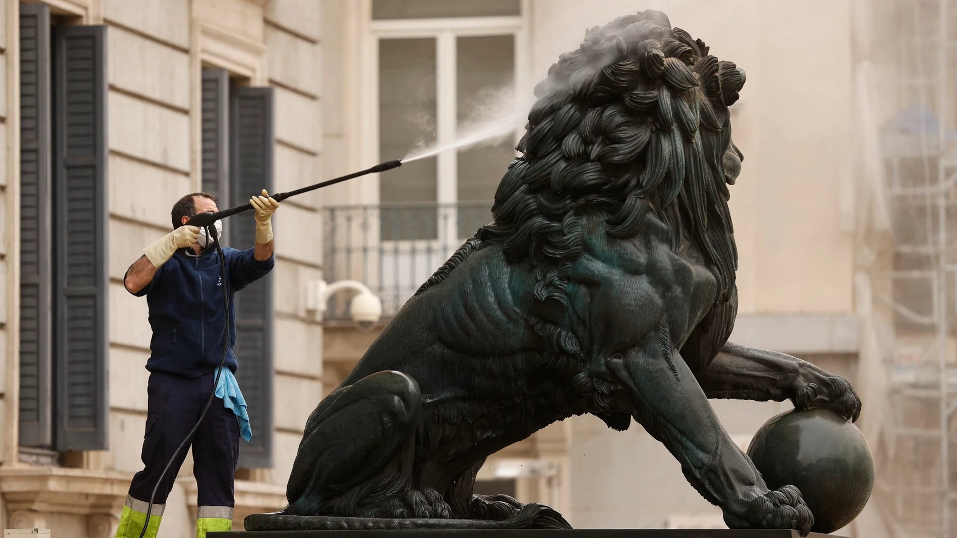 GRAF9353. MADRID, 15/03/2022.- Un operario utiliza agua a presión para limpiar uno de los leones del Congreso, este martes. Un "excepcional" episodio de polvo procedente del desierto del Sahara se registra este martes, intensificada su presencia debido a la lluvia, en varias provincias de la península Ibérica, un fenómeno que no se producía con esta intensidad desde hacía varias décadas. EFE/ Chema Moya